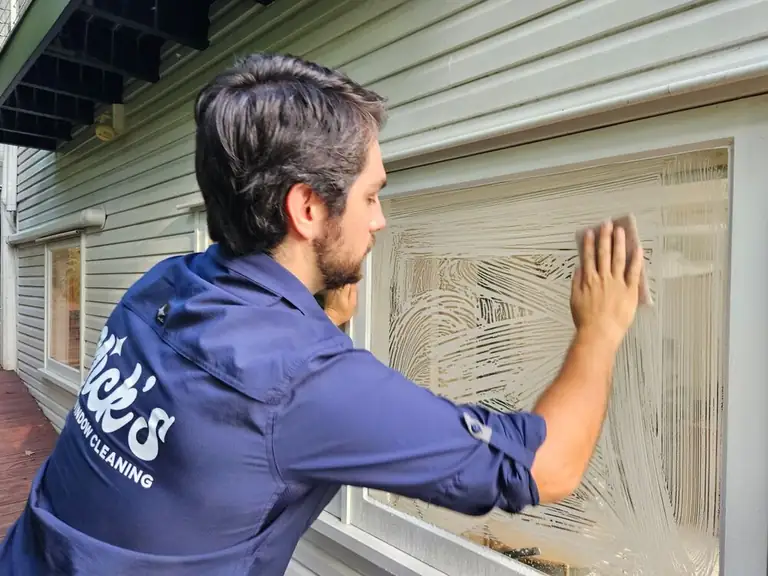 Technician washing a house window with a soapy applicator